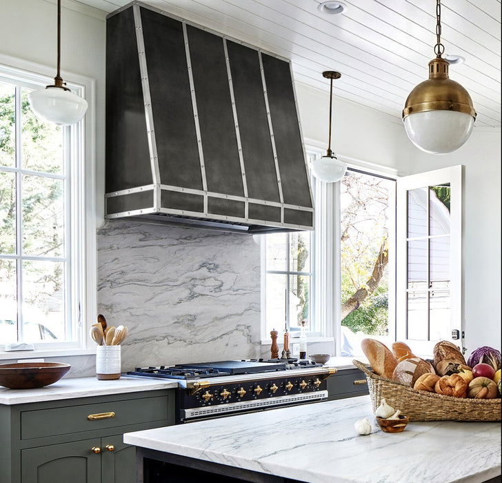 Handcrafted antique zinc custom kitchen range hood with angled design and brushed stainless steel straps and rivets at rangehoodmaster