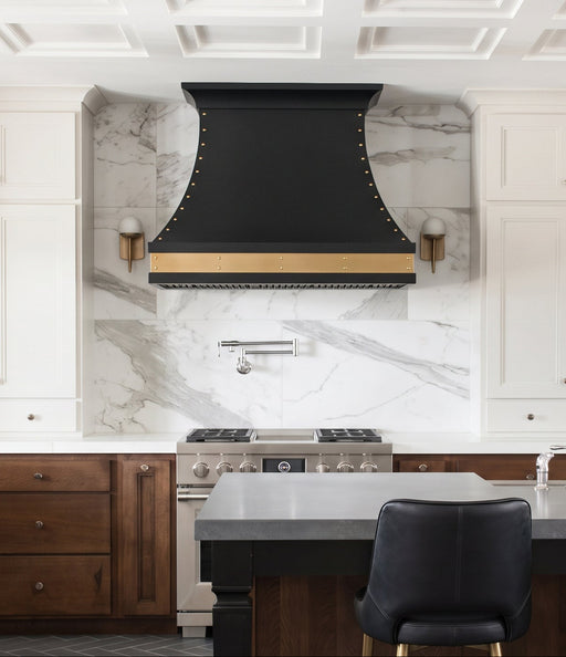 custom matte black curved kitchen range hood with brushed brass apron and rivets at Range Hood Master