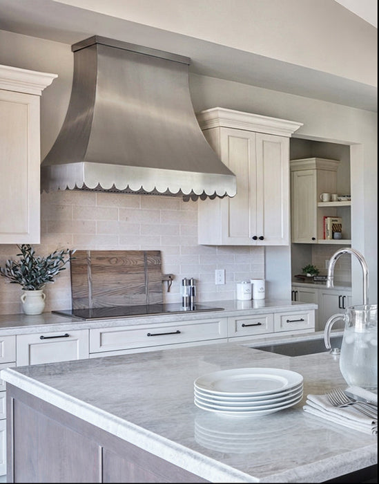 Brushed stainless steel range hood with scalloped apron and flat crown molding at rangehoodmaster