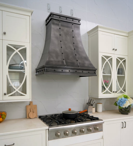 Custom antique blackened zinc curved range hood with stainless steel straps and rivets in industrial kitchen style