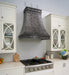 Custom antique blackened zinc curved range hood with stainless steel straps and rivets in industrial kitchen style