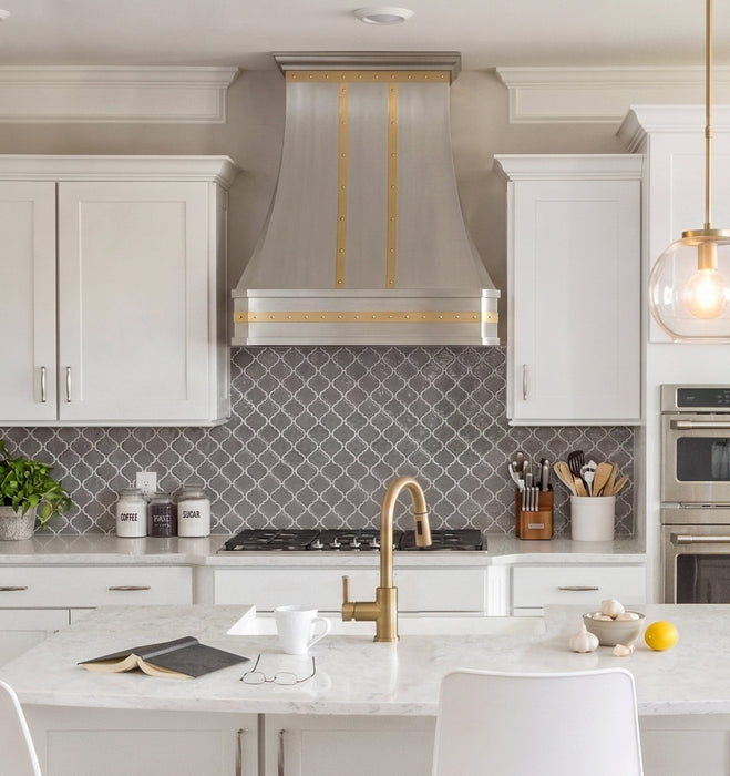 Modern stainless steel range hood with golden decorative straps, crown molding and rivets at rangehoodmaster