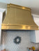 Custom brass range hood modern curved design with straps and rivets at RangeHoodMaster